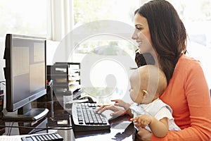 Hispanic mother with baby working in home office