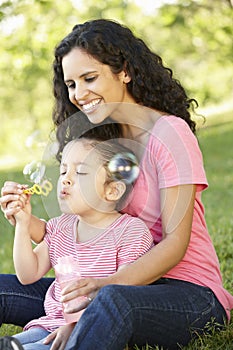 Hispanic Mother And Daughter Blowing BubblesIn Park