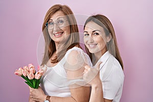 Hispanic mother and daughter holding pink tulips bouquet smiling happy and positive, thumb up doing excellent and approval sign