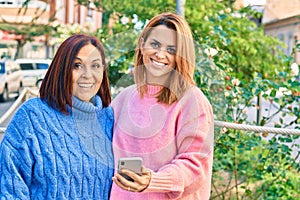 Hispanic mother and daughter smiling happy using smartphone at the park
