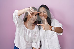 Hispanic mother and daughter together smiling making frame with hands and fingers with happy face
