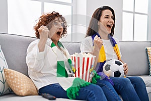 Hispanic mother and daughter watching football supporting team screaming proud, celebrating victory and success very excited with