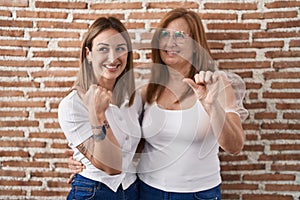 Hispanic mother and daughter wearing casual white t shirt smiling with happy face looking and pointing to the side with thumb up