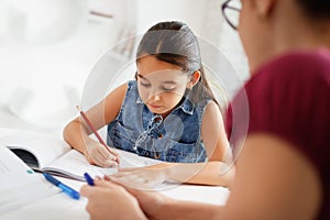 Hispanic Mother Helping Girl Doing School Homework At Home