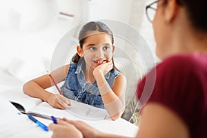 Hispanic Mother Helping Girl Doing School Homework At Home