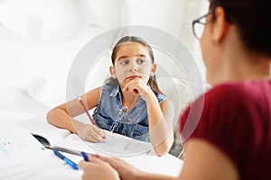 Hispanic Mother Helping Girl Doing School Homework At Home