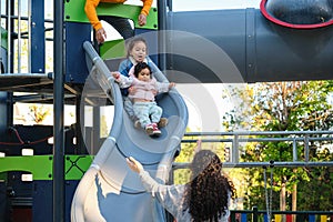 Hispanic parents playing with her children at the slide in a park.