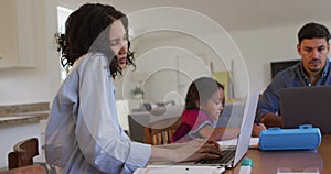 Hispanic parents sitting at table working with laptops and daughter drawing