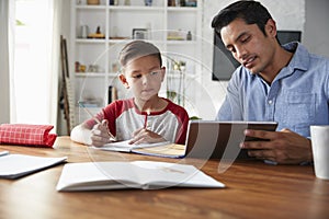Hispanic pre-teen boy sitting at table working with his home school tutor, using tablet computer photo