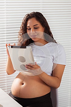 Hispanic pregnant woman using digital tablet while breakfast. Technology, pregnancy and maternity leave