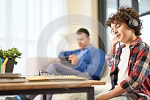 Hispanic school boy wearing headphones, preparing homework while sitting at the desk at home