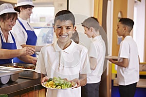 Hispanic schoolboy holds a plate of food in school cafeteria photo