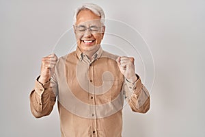 Hispanic senior man wearing glasses excited for success with arms raised and eyes closed celebrating victory smiling