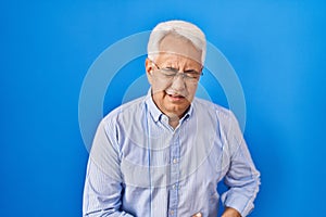 Hispanic senior man wearing glasses with hand on stomach because indigestion, painful illness feeling unwell