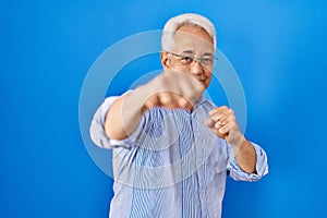 Hispanic senior man wearing glasses punching fist to fight, aggressive and angry attack, threat and violence