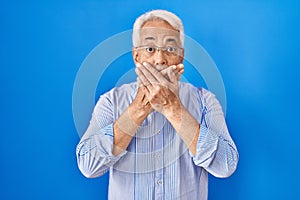 Hispanic senior man wearing glasses shocked covering mouth with hands for mistake
