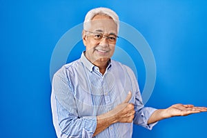 Hispanic senior man wearing glasses showing palm hand and doing ok gesture with thumbs up, smiling happy and cheerful