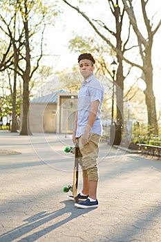 Hispanic skateboarder stands in the park looking far out over th