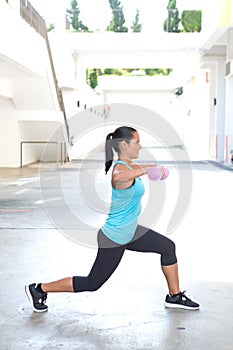 Hispanic sport woman doing lunges with two pink dumbbell, outdoor.