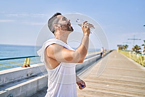 Hispanic sports man wearing workout style drinking water to stay hydrated outdoors on a sunny day