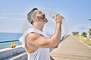 Hispanic sports man wearing workout style drinking water to stay hydrated outdoors on a sunny day