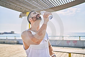 Hispanic sports man wearing workout style drinking water to stay hydrated outdoors on a sunny day