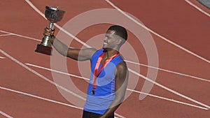 Hispanic sportsman with gold medal on chest holding cup, realizing his victory