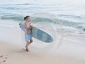 Hispanic surfer walking on the beach with his surfboard