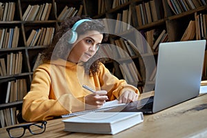 Hispanic teen girl student wear headphones watching webcast class making notes.