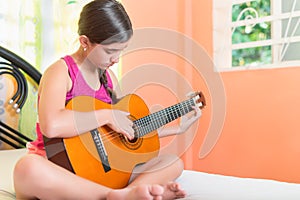 Hispanic teenage girl playing guitar at home
