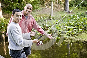 Hispanic teenager and father fishing in pond