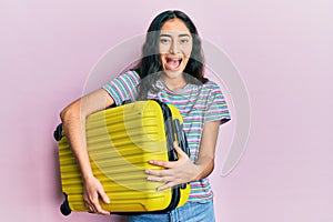 Hispanic teenager girl with dental braces holding cabin bag celebrating crazy and amazed for success with open eyes screaming