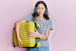 Hispanic teenager girl with dental braces holding cabin bag clueless and confused expression