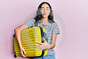 Hispanic teenager girl with dental braces holding cabin bag looking at the camera blowing a kiss being lovely and sexy