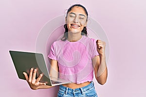 Hispanic teenager girl with dental braces holding and using computer laptop screaming proud, celebrating victory and success very