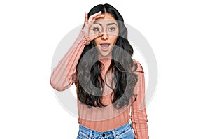 Hispanic teenager girl with dental braces wearing casual clothes doing ok gesture shocked with surprised face, eye looking through