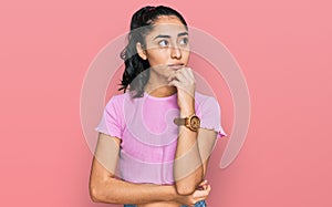Hispanic teenager girl with dental braces wearing casual clothes with hand on chin thinking about question, pensive expression