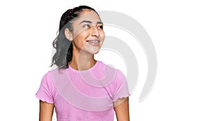 Hispanic teenager girl with dental braces wearing casual clothes looking away to side with smile on face, natural expression