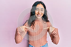 Hispanic teenager girl with dental braces wearing casual clothes looking confident with smile on face, pointing oneself with