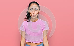 Hispanic teenager girl with dental braces wearing casual clothes making fish face with lips, crazy and comical gesture