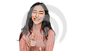 Hispanic teenager girl with dental braces wearing casual clothes pointing fingers to camera with happy and funny face
