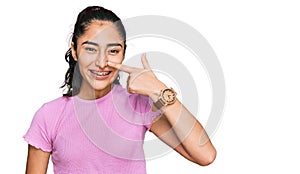 Hispanic teenager girl with dental braces wearing casual clothes pointing with hand finger to face and nose, smiling cheerful