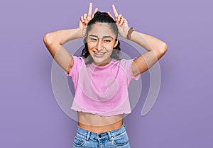 Hispanic teenager girl with dental braces wearing casual clothes posing funny and crazy with fingers on head as bunny ears,