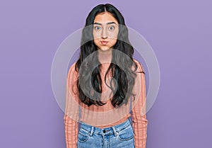 Hispanic teenager girl with dental braces wearing casual clothes puffing cheeks with funny face