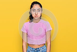 Hispanic teenager girl with dental braces wearing casual clothes puffing cheeks with funny face