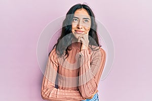Hispanic teenager girl with dental braces wearing casual clothes serious face thinking about question with hand on chin,