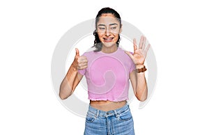 Hispanic teenager girl with dental braces wearing casual clothes showing and pointing up with fingers number six while smiling