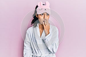 Hispanic teenager girl with dental braces wearing sleep mask and robe looking stressed and nervous with hands on mouth biting