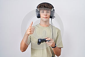 Hispanic teenager playing video game holding controller doing happy thumbs up gesture with hand
