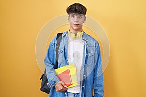 Hispanic teenager wearing student backpack and holding books with a happy and cool smile on face